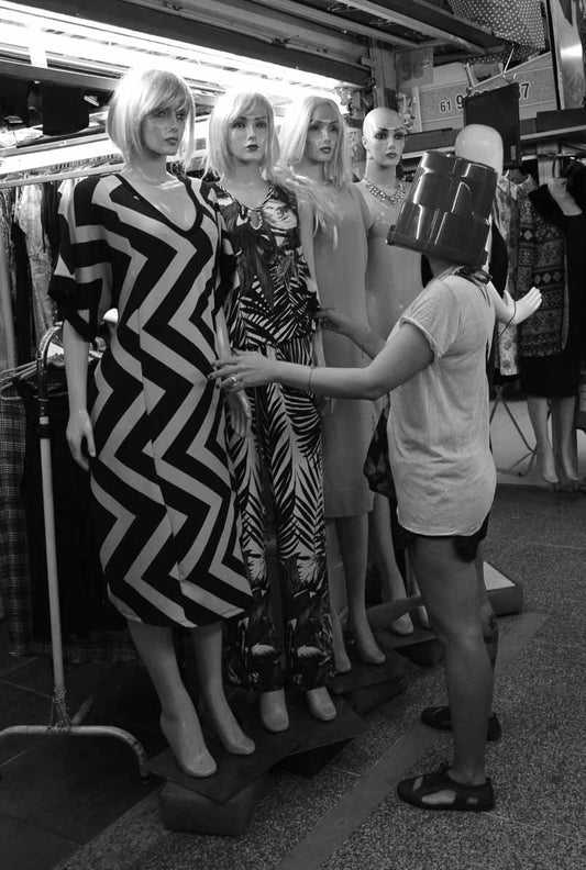 Mulher Baldia observa manequins em loja de roupas.